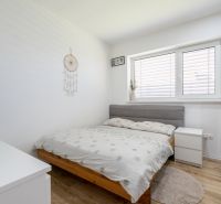 Bright bedroom with a bed, wood-patterned floor, and a dreamcatcher on the wall.