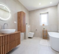A bathroom in a family house with a bathtub, a wall-hung toilet, and wooden decor furniture.