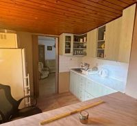 Interior of a cottage with a kitchen unit, refrigerator, and wooden decor flooring.