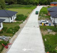 A road with family houses in the village of Prašník, surrounded by greenery and buildings.
