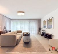 Living room in a 4-room apartment with a beige sofa, wooden cabinets, and large windows.