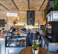 A café with brick walls, a counter with a menu of food and drinks, plants in the gastro area.