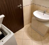 A bathroom with a washing machine, sink, and beige tiles in a 3-room apartment.