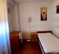 A room in a 3-room apartment with a wooden decor floor, a bed, and a table.