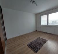A bright room with a carpet and wood-patterned flooring in a three-room apartment.