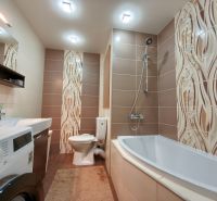 Bathroom in a 3-room apartment with a bathtub, washing machine, and brown tiles.