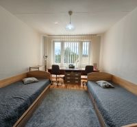 A room in a 3-room apartment with two beds, a table, and a floor with a wooden decor.