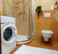 A bathroom with a washing machine, shower, and toilet in a 2-room apartment.