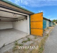 Open garages in Detva with an asphalt access road and blue sky.