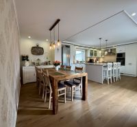 A kitchen in a family house with an island, a dining table, and a floor with a wooden decor.