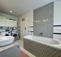 A bathroom in a family house with a bathtub, washing machine, sinks, and storage cabinets.