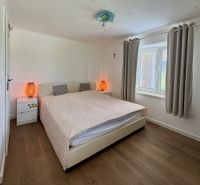 Bedroom in a family house with a bed, lamps, and wooden decor flooring.