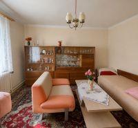 A room in a family house with a sofa, a display cabinet, and a carpet with a floral pattern.