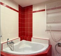A bathroom in a 3-room apartment with a corner bathtub and red tiles.