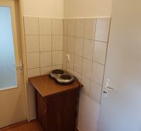 A kitchenette in a studio apartment with an electric stove and a cabinet, tiled.