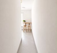 A narrow hallway in a 2-room apartment with tiles leading to a small table and chairs.