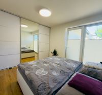 Bedroom in a family house with a bed, built-in wardrobe, and wooden decor flooring.