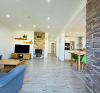 Living room with a fireplace, wooden decor flooring, and a kitchenette in a family house.