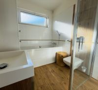 A bathroom in a family house with a bathtub, a shower corner, and a floor with a wooden decor.