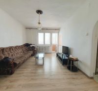 Living room with a brown sofa, television, and wood-patterned flooring in a three-room apartment.