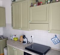 A kitchen in a holiday apartment with white tiles and green cabinets.