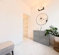 A bright hallway in a 3-room apartment with white walls, a green plant, and a dresser.