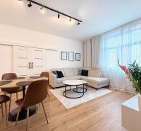 Living room in a three-room apartment with a sofa, dining table, and wooden decor flooring.