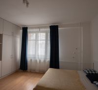 A room in a one-bedroom apartment with a bed, storage spaces, and a floor with a wooden decor.