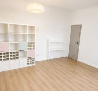 A room in a 3-room apartment with a wooden decor floor and a white shelf.
