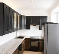 A kitchen in a 3-room apartment with black cabinets, white walls, and a granite countertop.