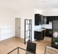 Open kitchen with black cabinets, wood-patterned flooring, and a table in a three-room apartment.