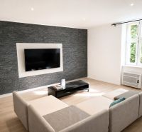 Living room in a 3-room apartment with a gray stone wall and a wooden decor floor.