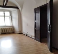 Interior of commercial premises with wood-effect flooring, older radiators, arched ceiling.