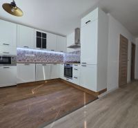 A kitchen in a 3-room apartment with a wood-patterned floor and white cabinets.