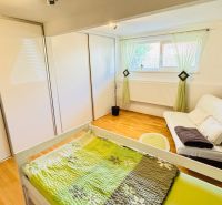 A bedroom in a family house with a wooden decor floor, a sofa, and a built-in wardrobe.