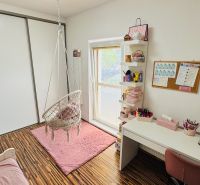 Children's room with a rocking chair, pink carpet, and wooden decor flooring.