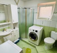 A bathroom in a family house with a washing machine, shower, and green tiles.