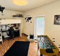 A room with a bunk bed and a foosball table, floor with wood decor.
