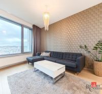 Living room in a 2-room apartment with a sofa, table, plant, and wooden decor flooring.