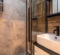 A bathroom with a sink, dark fixtures, and walls in natural stone and wood decor.