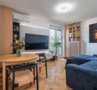 Living room in a 3-room apartment with a wooden decor floor, a comfortable sofa, and a television.