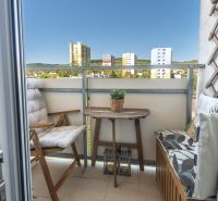 A balcony with a view of the housing estate, wooden furniture, and greenery. Bratislava - Rača, Sadmelijská.