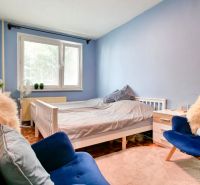 A bedroom in a two-room apartment with blue walls, white furniture, and armchairs.