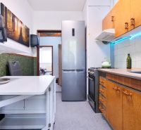 A kitchen of a 2-room apartment with a wooden decor, a kitchen sink, and an appliance.