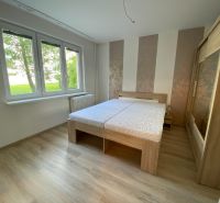 A bedroom in a two-room apartment with a wood-patterned floor and large windows.