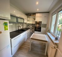 A bright kitchen with white cabinets and a table that has a wood-patterned floor.