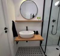 A bathroom in a 3-room apartment with a round mirror, a shower, and decorative flooring.