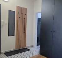 A hallway in a 3-room apartment with a black wardrobe, a coat rack, and white walls.