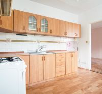 A kitchen in a 3-room apartment with a light-colored kitchen unit and a floor with a wood design.