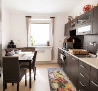 A kitchen in a family house with dark furniture, a decorative rug, and natural daylight.